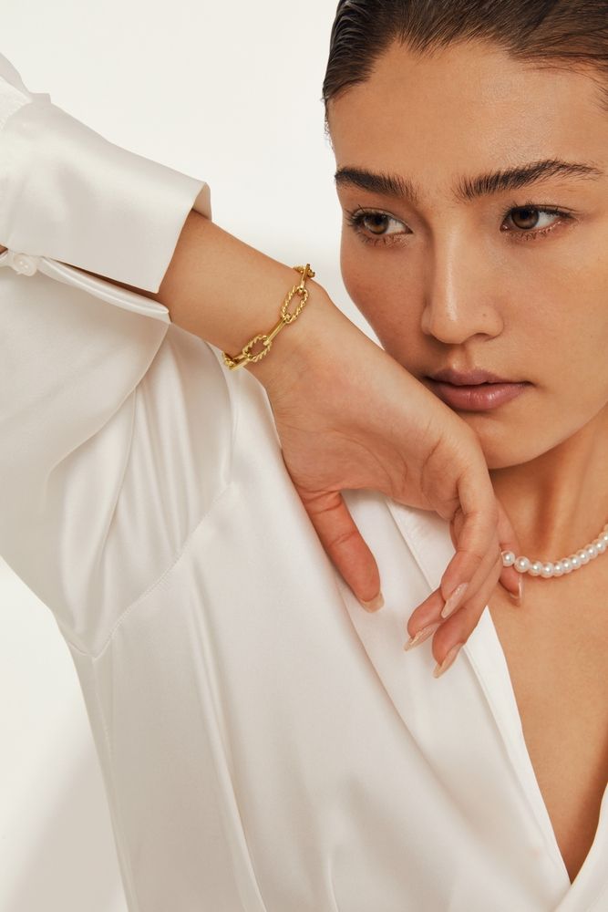 Model wearing a gold link bracelet and pearl necklace